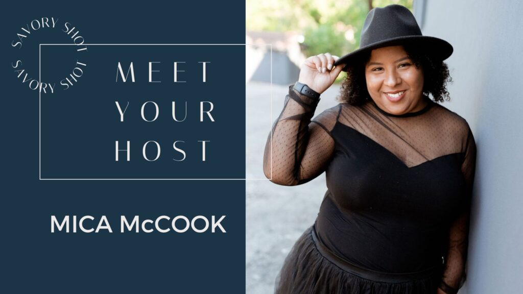 African American woman wearing black dress and black hat leaning against grey wall.