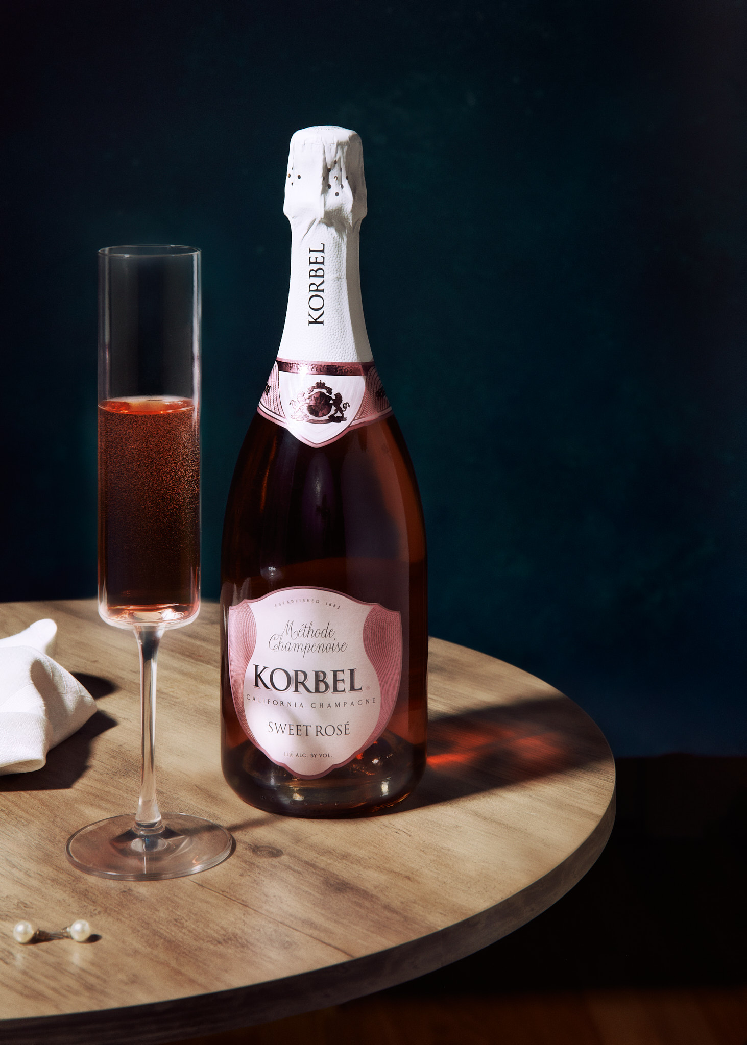 Bottle of Korbel Sweet Rosé California Champagne with a filled champagne flute on a wooden table.