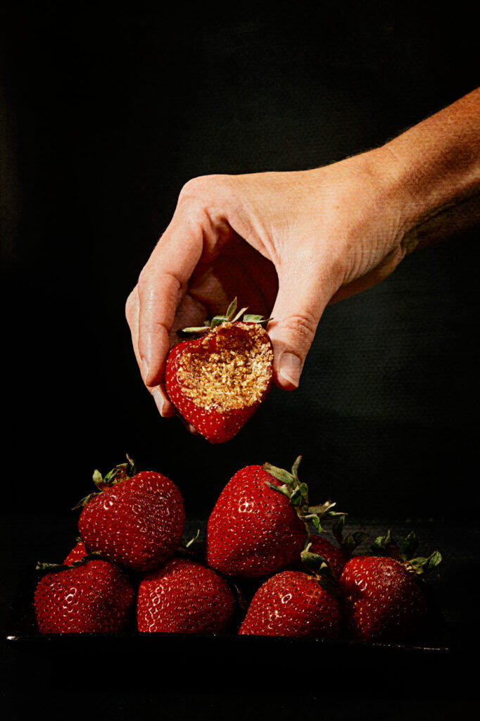 hand holding strawberry with bite and gold glitter inside